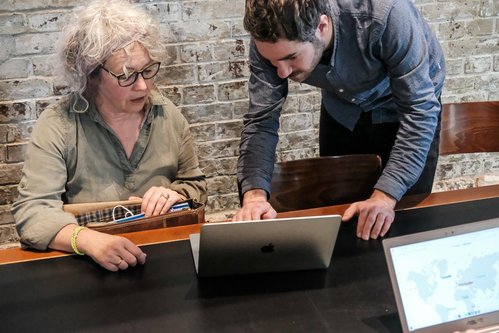 Zwei Personen sind über einen Laptop gebeugt und sprechen miteinander