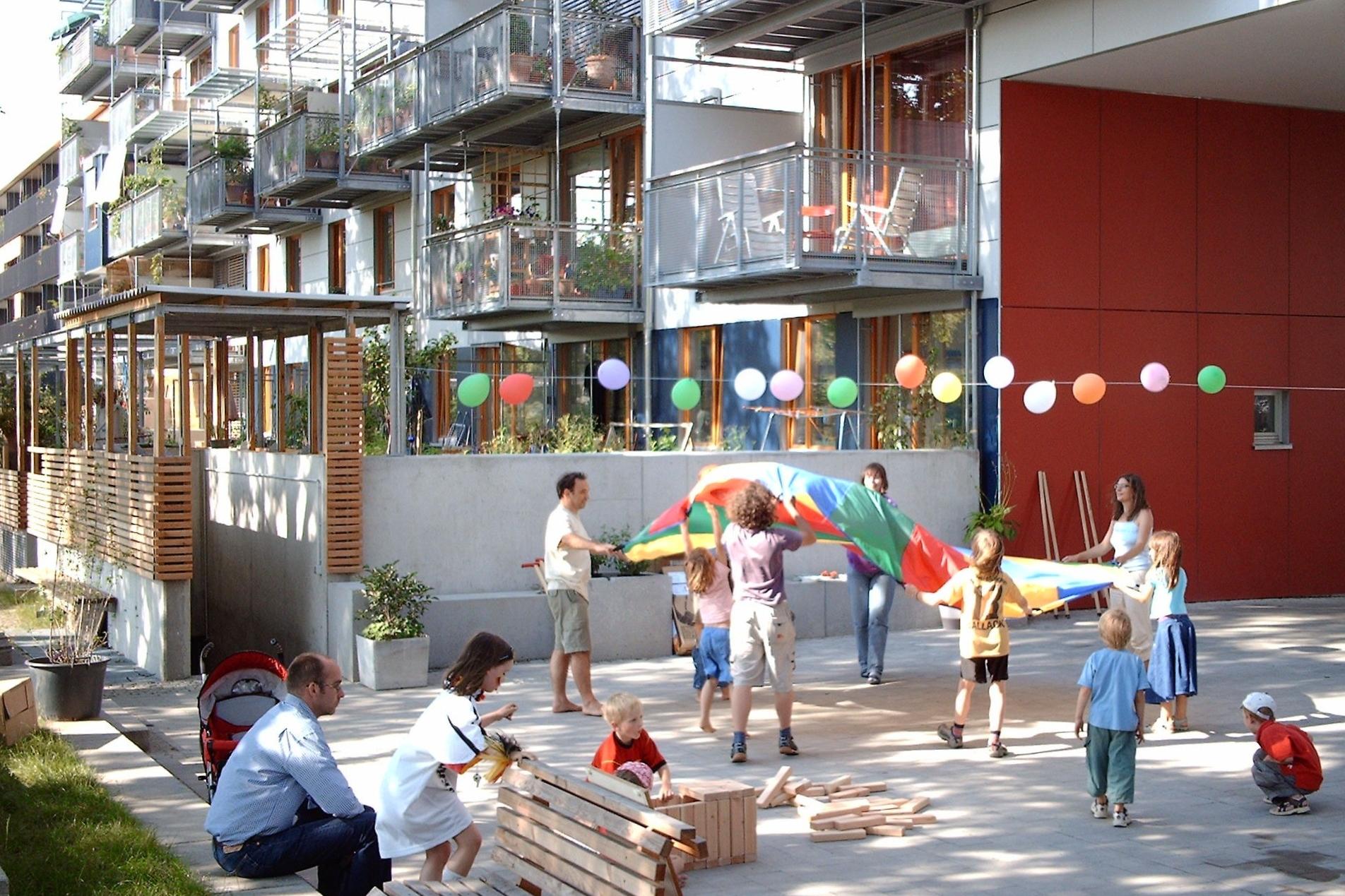 Auf dem Innenhof eines modernen Mehrfamilien-Hauses spielen Kinder und Erwachsene.